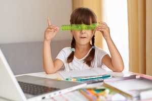 playful-female-child-white-t-shirt-sitting-table-front-opened-notebook-covering-eyes-with-green-ruler-distance-education-quarantine-pointing-finger-up-having-idea - Crossroads Family Therapy playful-female-child-white-t-shirt-sitting-table-front-opened-notebook-covering-eyes-with-green-ruler-distance-education-quarantine-pointing-finger-up-having-idea